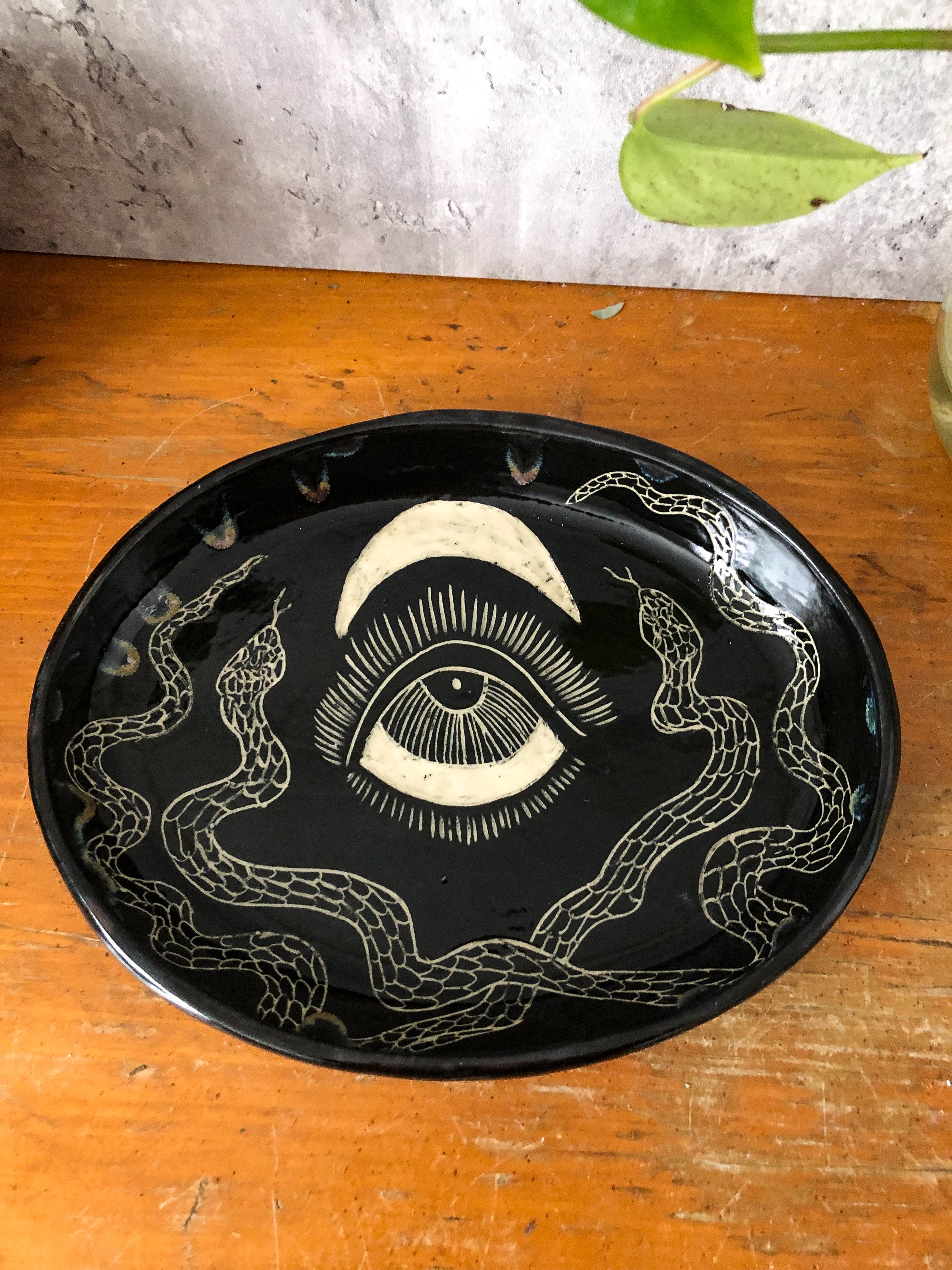 It's all about the details with this delightful serpent platter: two snakes sit opposite of each other framing out an eye underneath a crescent moon. Drippy oil-slick glaze oozes down from the rim. 